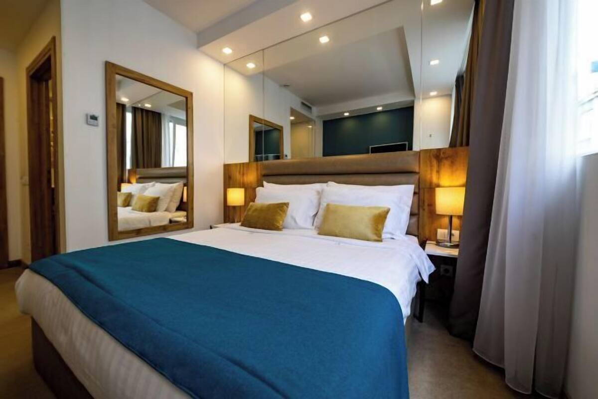 A hotel room with a large bed, bedside lamps, a mirror, and a view of the outside.