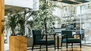 A modern indoor seating area with two dark green chairs, a small round table, and a large potted plant.