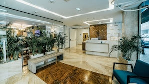 A modern lobby with a marble reception desk, seating area, and potted plants.