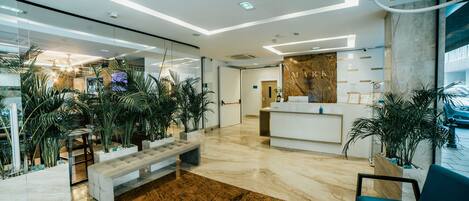 A modern lobby with a marble reception desk, seating area, and potted plants.