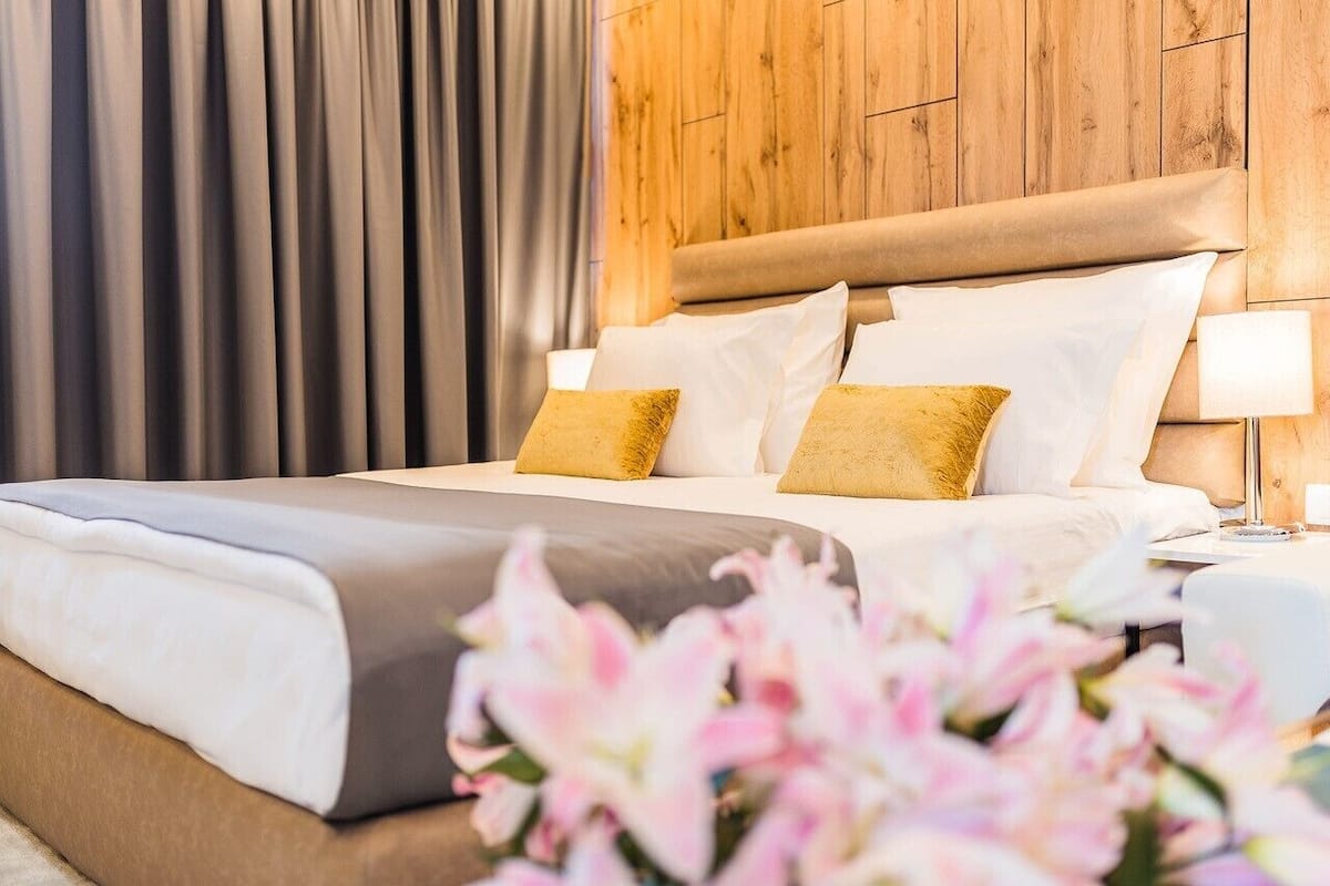 A neatly made bed with white and gold pillows, a wooden headboard, and a bedside lamp.