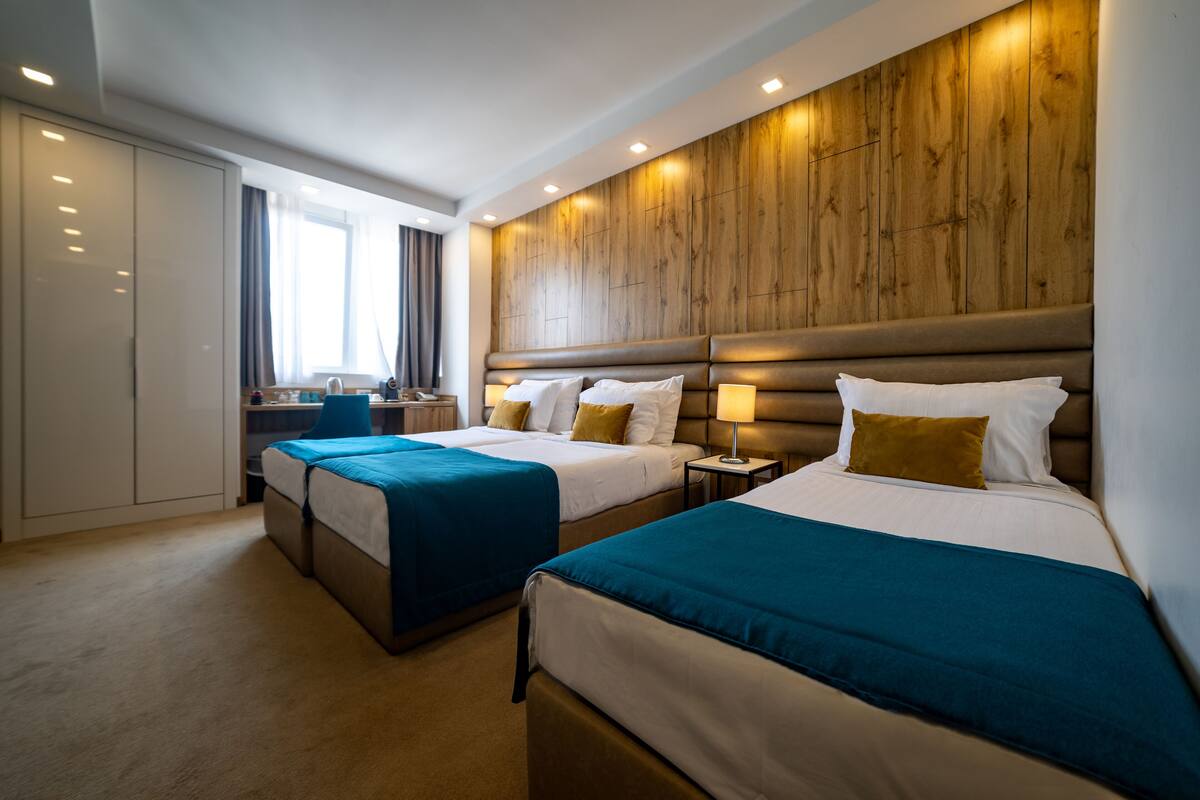 A hotel room with two beds, a wooden headboard, a desk, and a wardrobe.