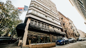 A Mark Hotel with a modern facade, large windows, and a parking area with cars.