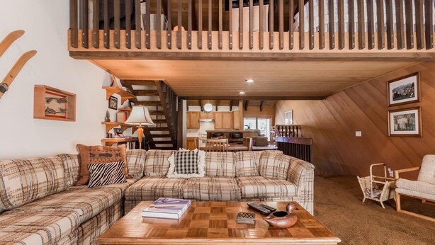 A cozy living room with a checkered sofa, a wooden coffee table, and a loft area above. - Snowcreek 97 - Phase I (Mammoth Lakes)