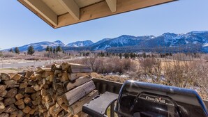 A covered outdoor area with a grill, a stack of firewood, and a view of snow-capped mountains. - Snowcreek 97 - Phase I (Mammoth Lakes)