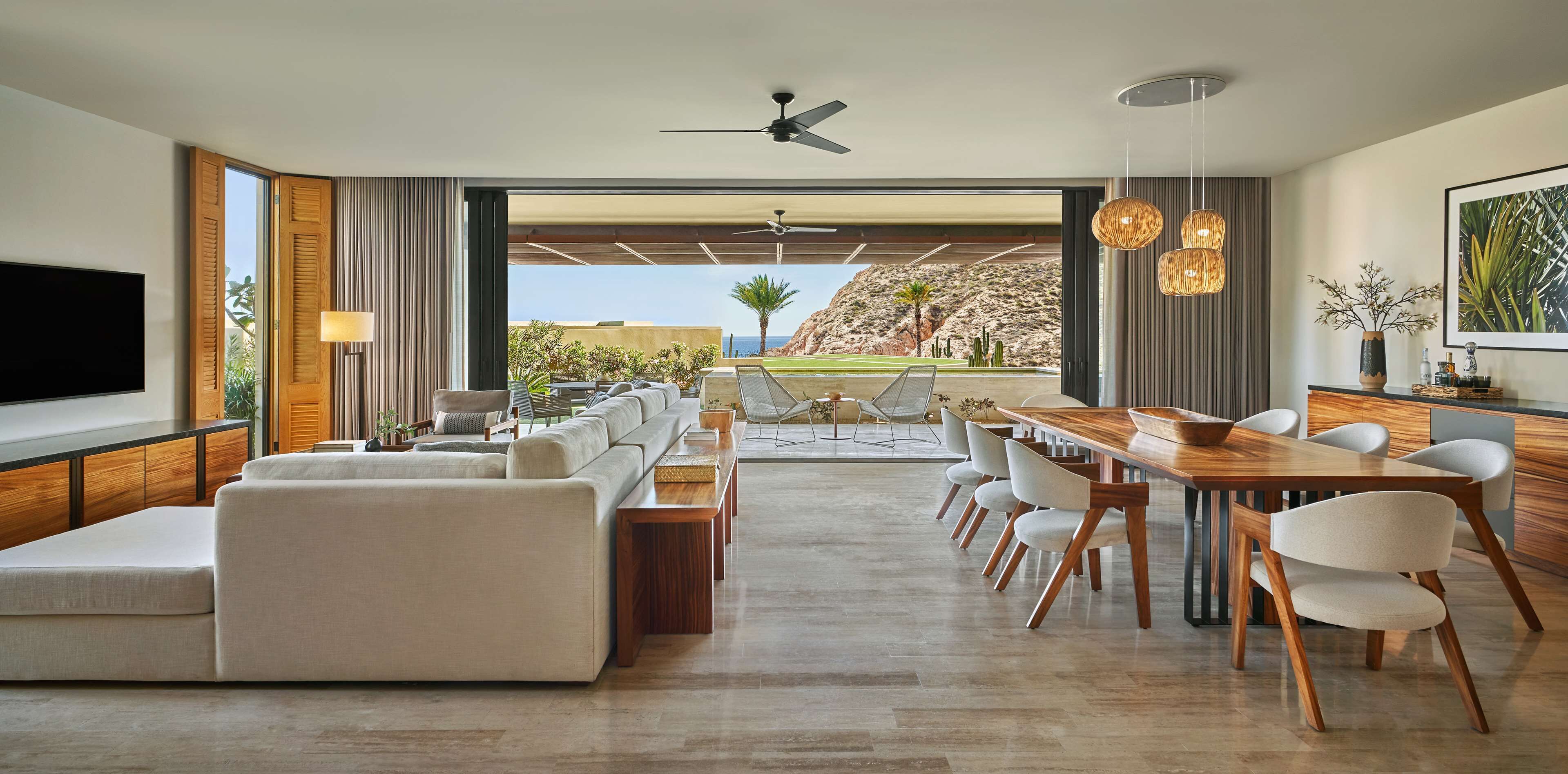 A modern living room with a large TV, comfortable seating, a dining area, and a view of a mountainous landscape.