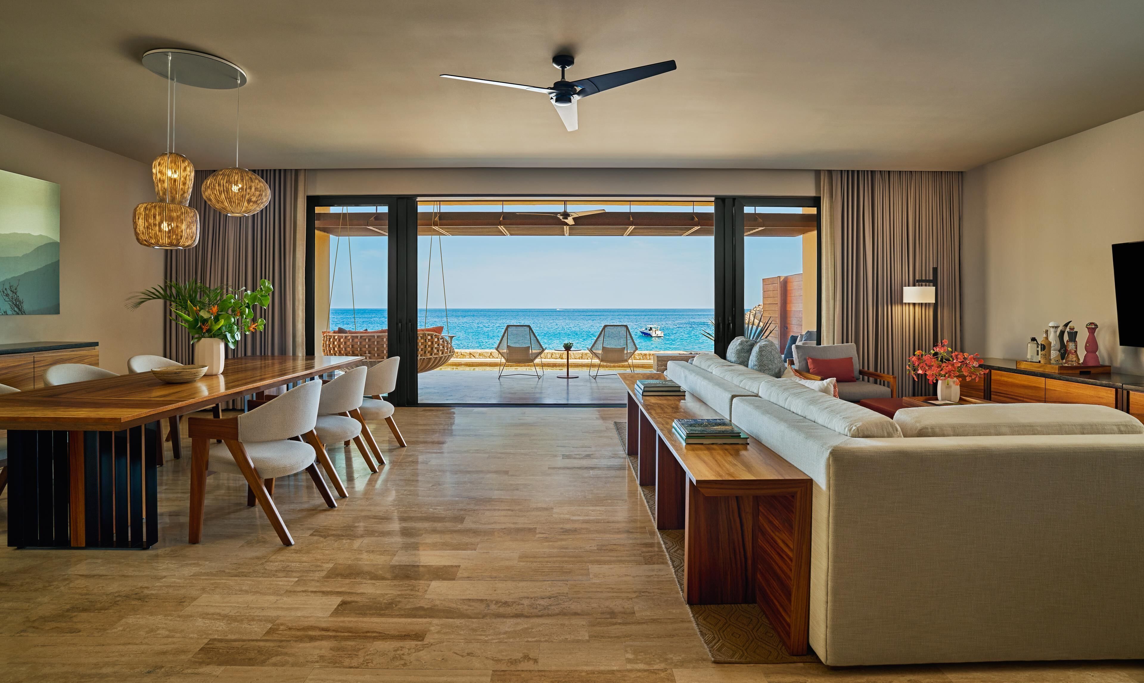 A modern living room with a view of the sea, a dining area, and a seating area with a sofa and chairs.