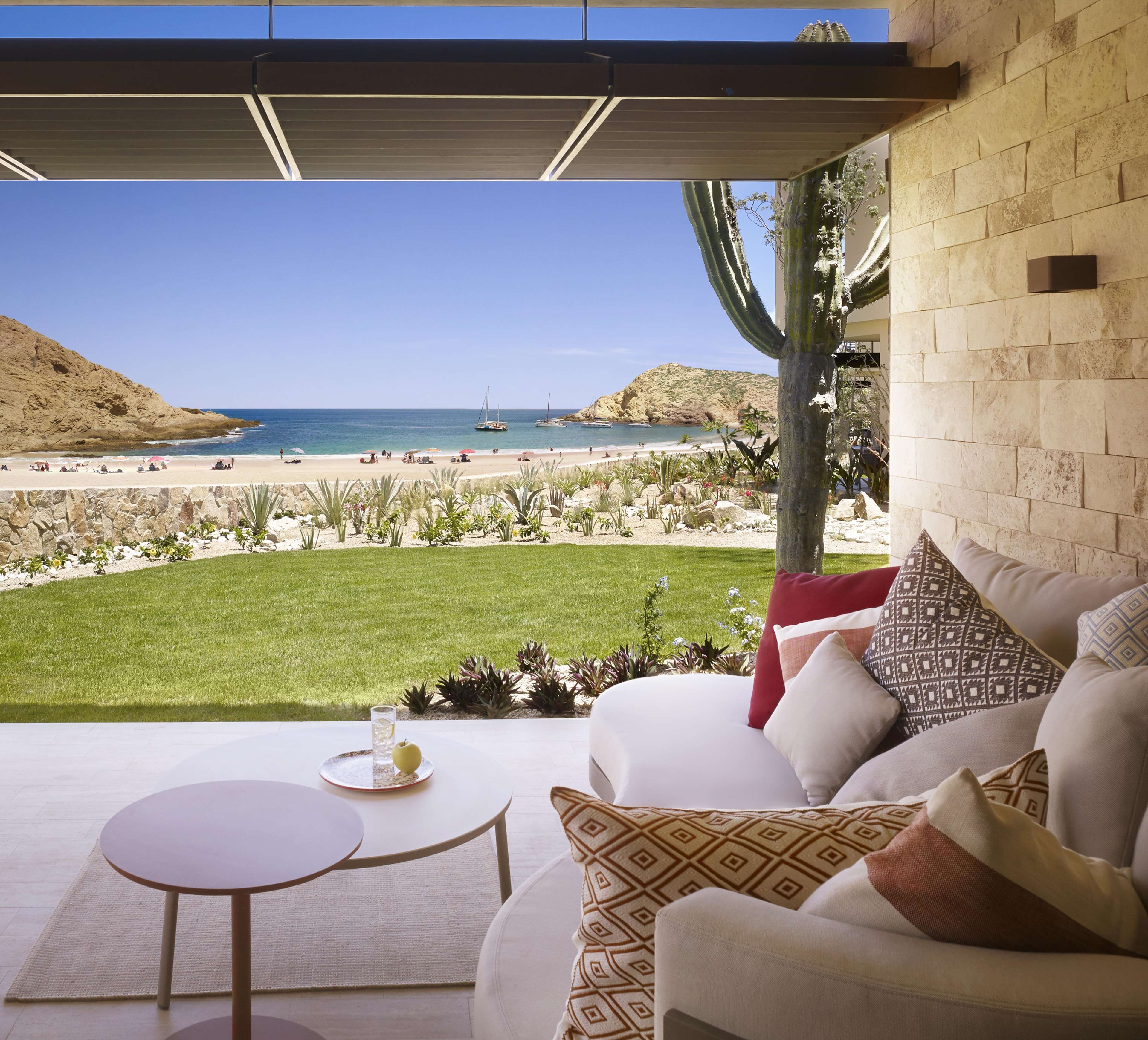 Un patio con vista a la playa, un cactus, y una mesa con un vaso de agua y una manzana.