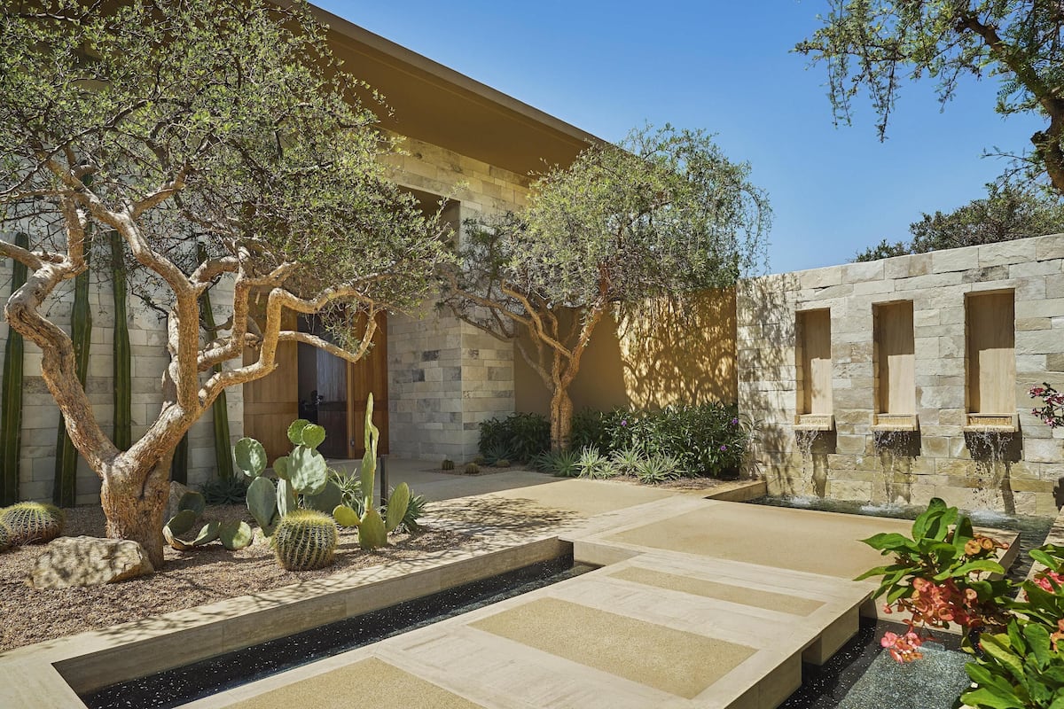 A courtyard with cacti, a stone wall, and a water feature.