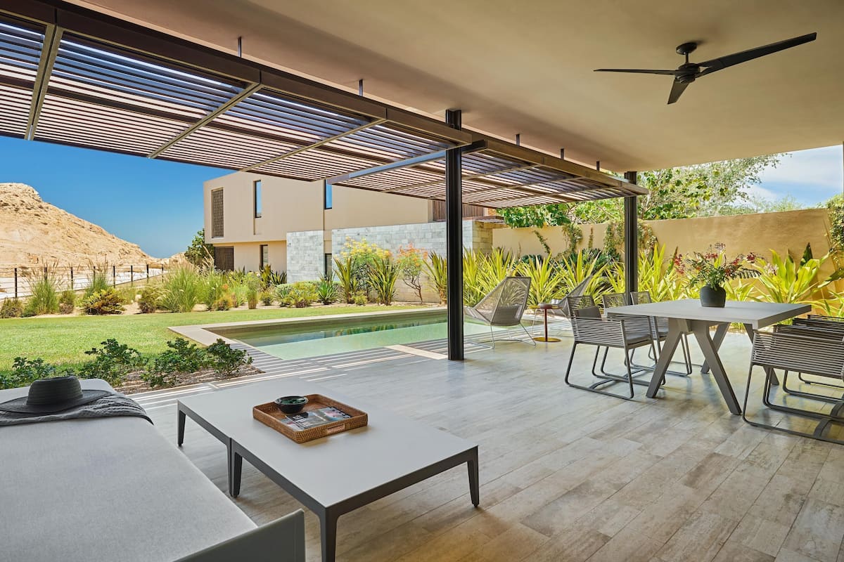 A modern outdoor patio with a pool, seating area, and a view of a desert landscape.