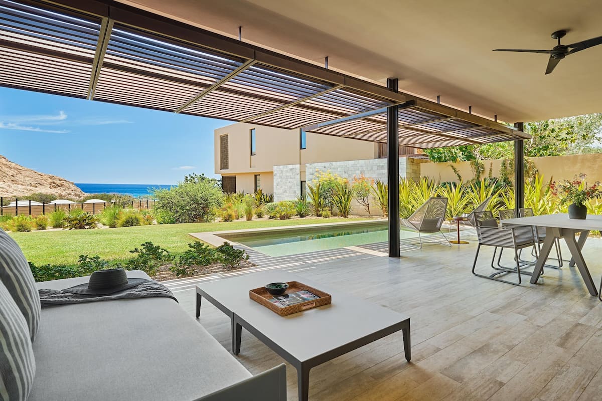 A modern outdoor patio with a pool, seating, and a view of the sea.