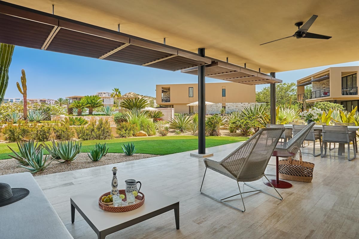 A modern outdoor patio with a dining area, a lounge chair, and a ceiling fan.