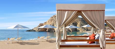 A beach with a canopy bed, lounge chairs, and umbrellas.