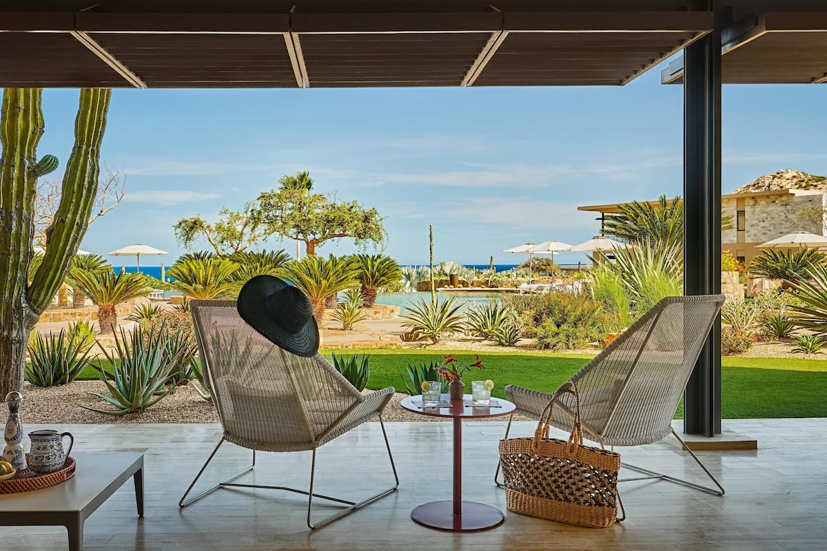 A patio with wicker chairs, a table, and a view of a pool and beach.