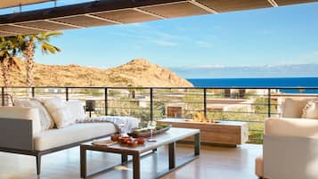 Uma área externa moderna para relaxar, com sofá, poltronas e mesa de centro, com vista para uma paisagem montanhosa e o mar.