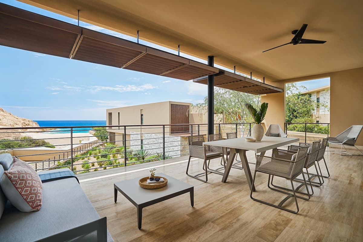 A balcony with a table and chairs, a sofa, and a view of the beach and ocean.