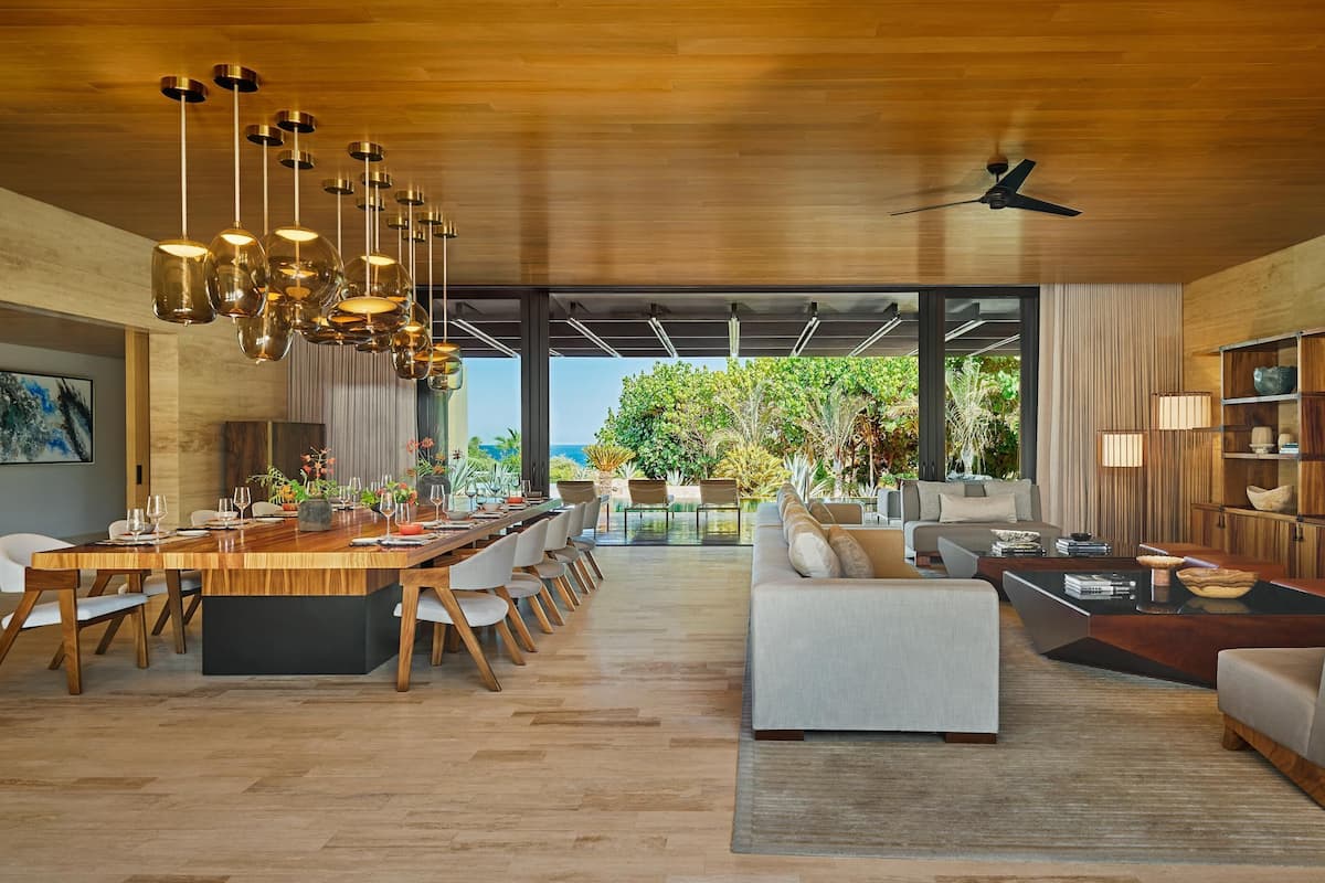 A spacious living area with a wooden ceiling, a dining table set for six, and a large sofa.