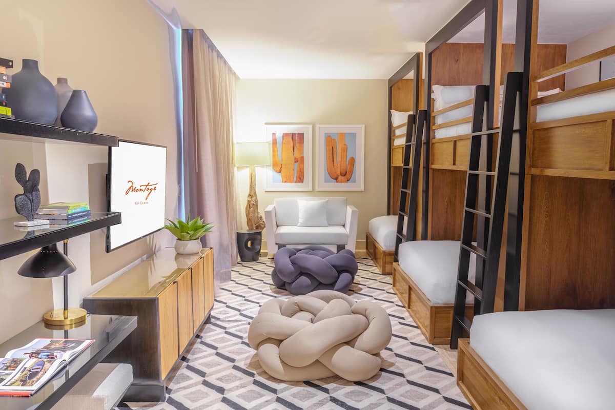A modern hotel room with a sofa, a bed, a wooden wardrobe, a TV, and artwork on the wall.