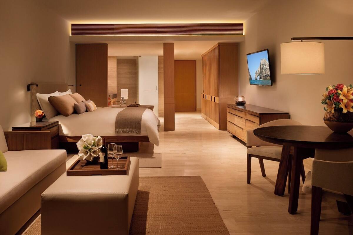 A modern hotel room with a bed, a sofa, a dining table, and a TV.