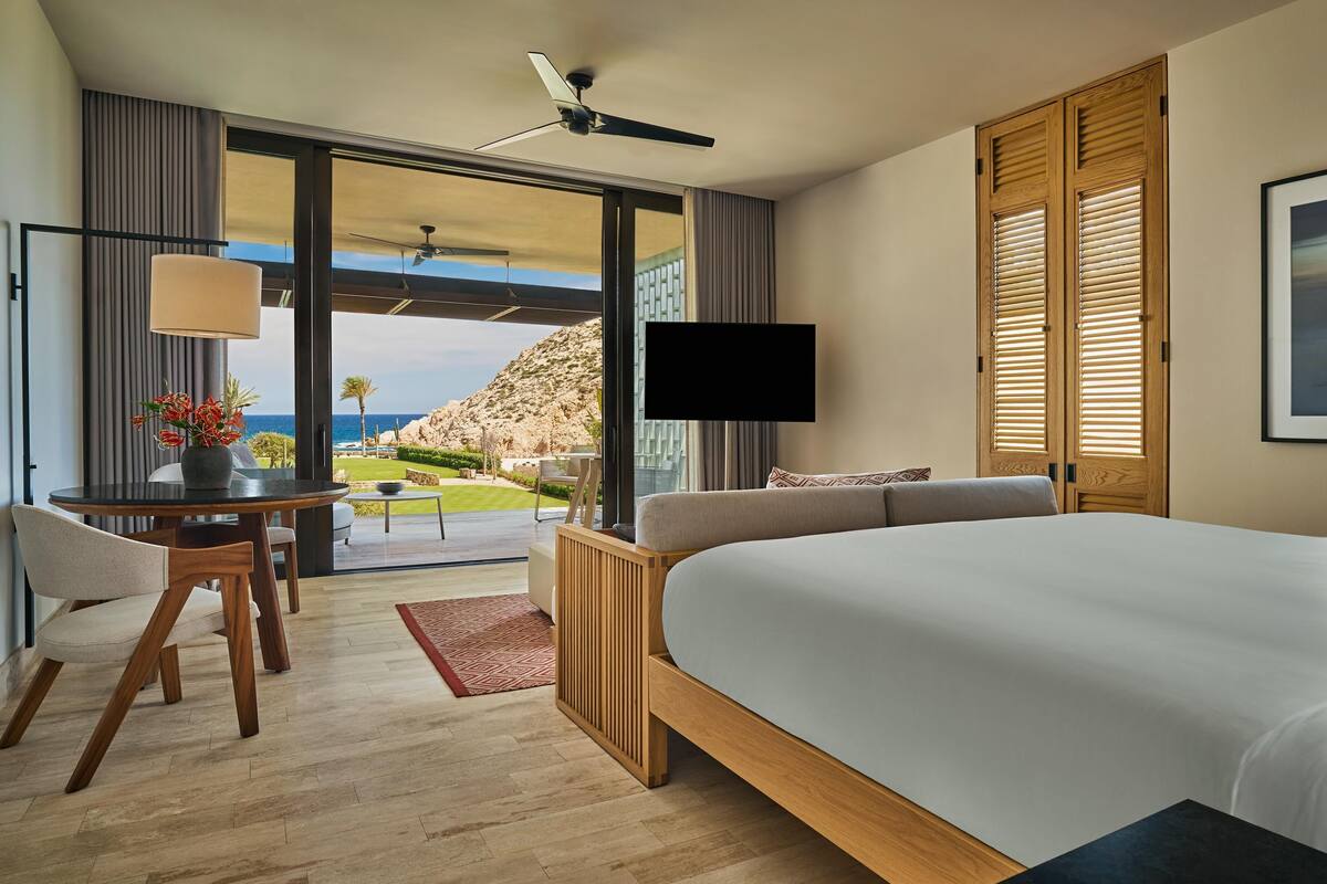 A hotel room with a bed, a desk with a lamp, a TV, and a view of the ocean.