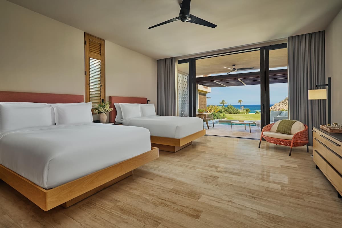 A hotel room with two beds, a sofa, a dining table, and a view of the ocean.