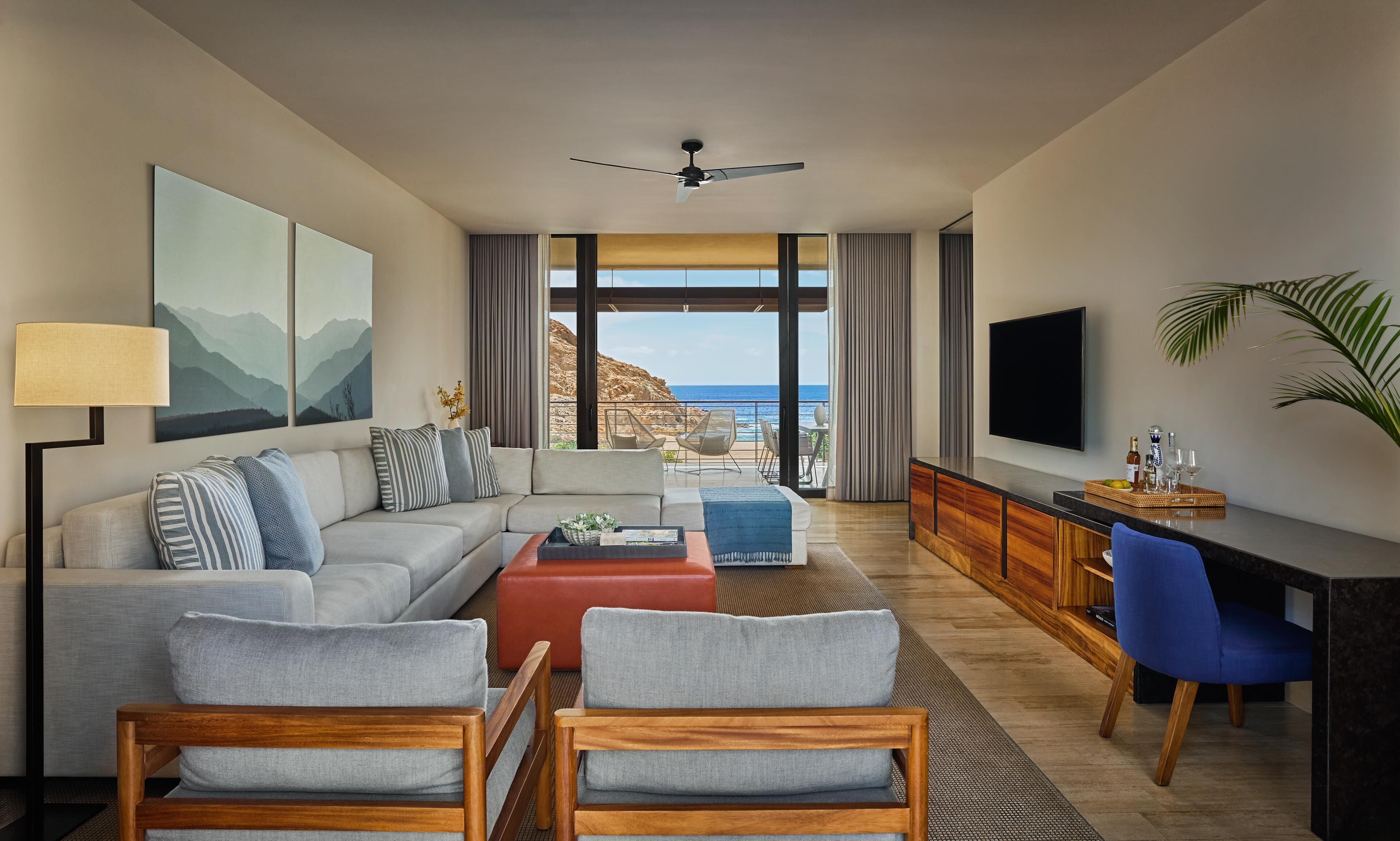 A modern living room with a sofa, chairs, a coffee table, a TV, and a view of the ocean.