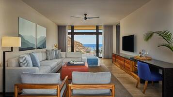 A modern living room with a sofa, chairs, a coffee table, a TV, and a view of the ocean.