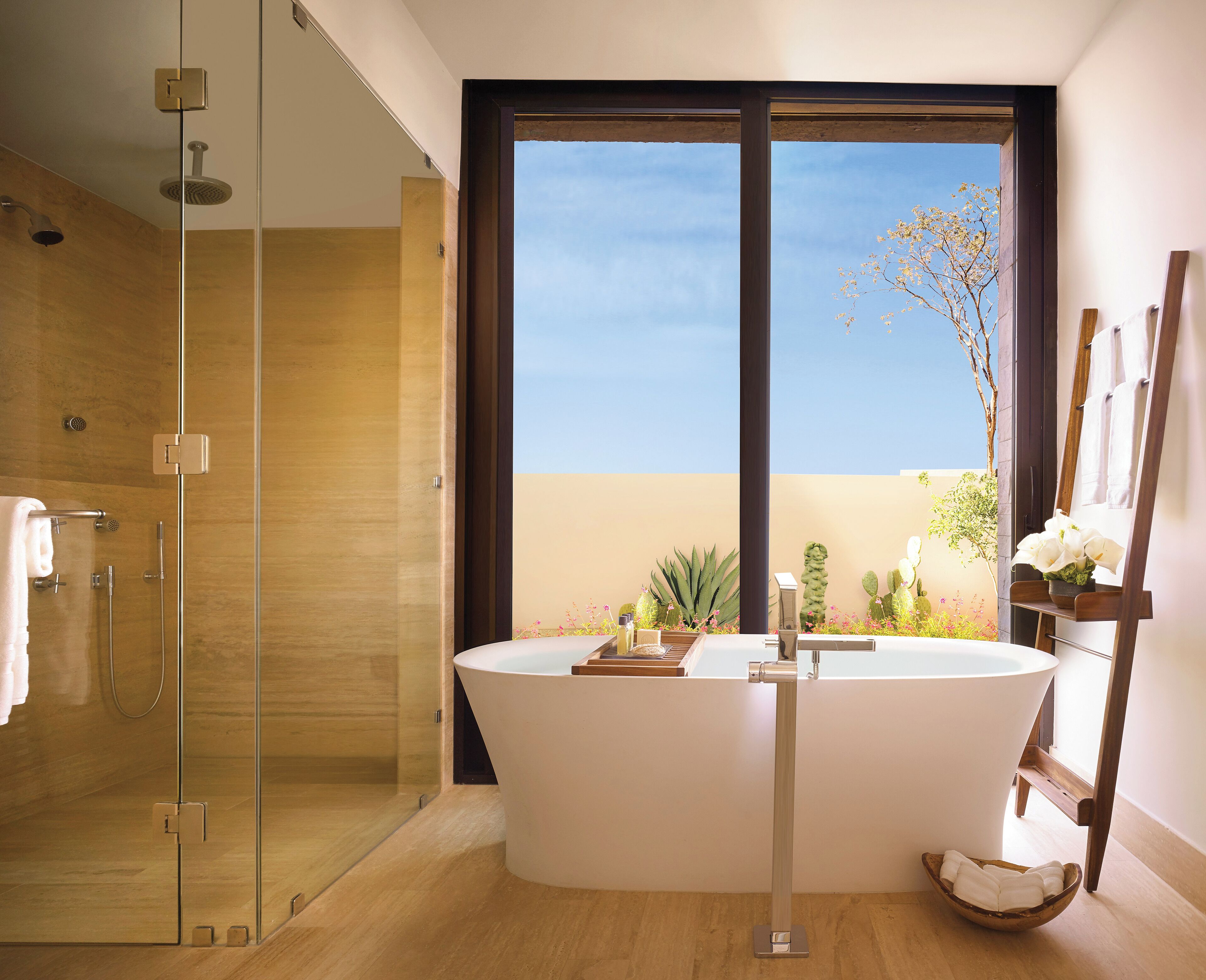 A modern bathroom with a freestanding bathtub, a glass-enclosed shower, and a large window offering a view of the outdoors.