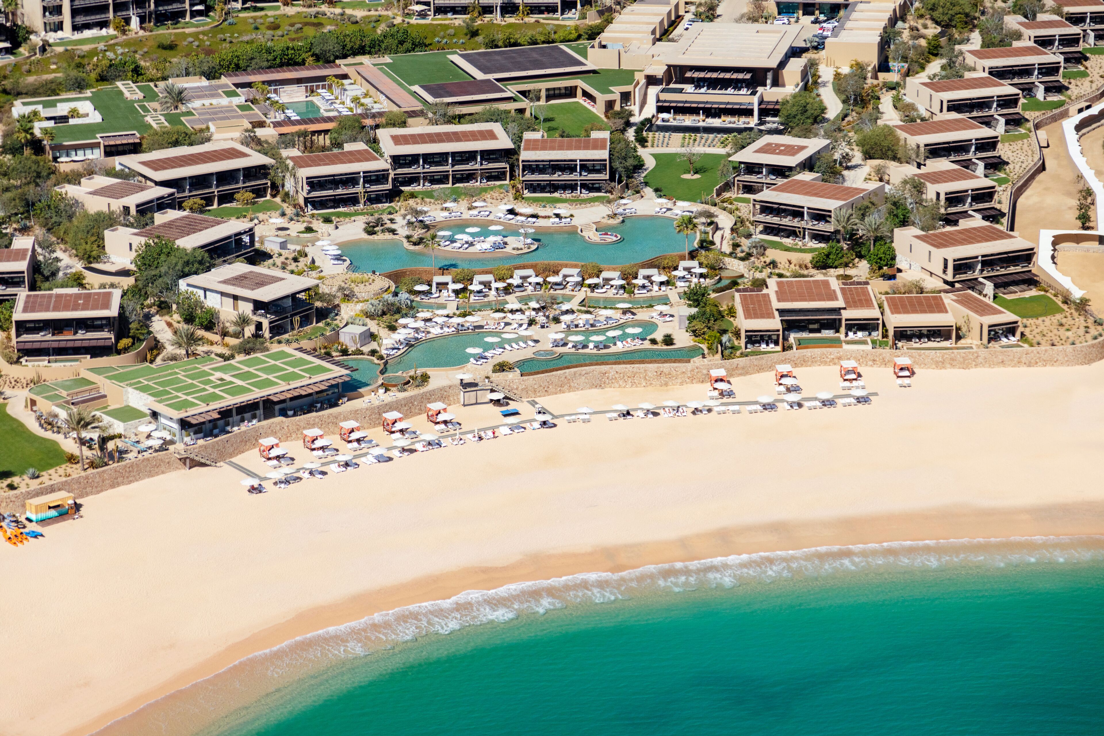 An aerial view of a resort with multiple buildings, a large pool area, and a beach.