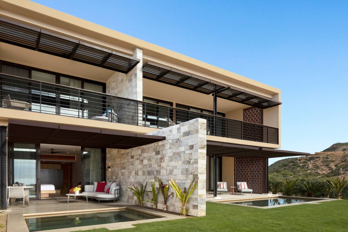 A modern two-story house with a balcony, a swimming pool, and a well-maintained lawn.