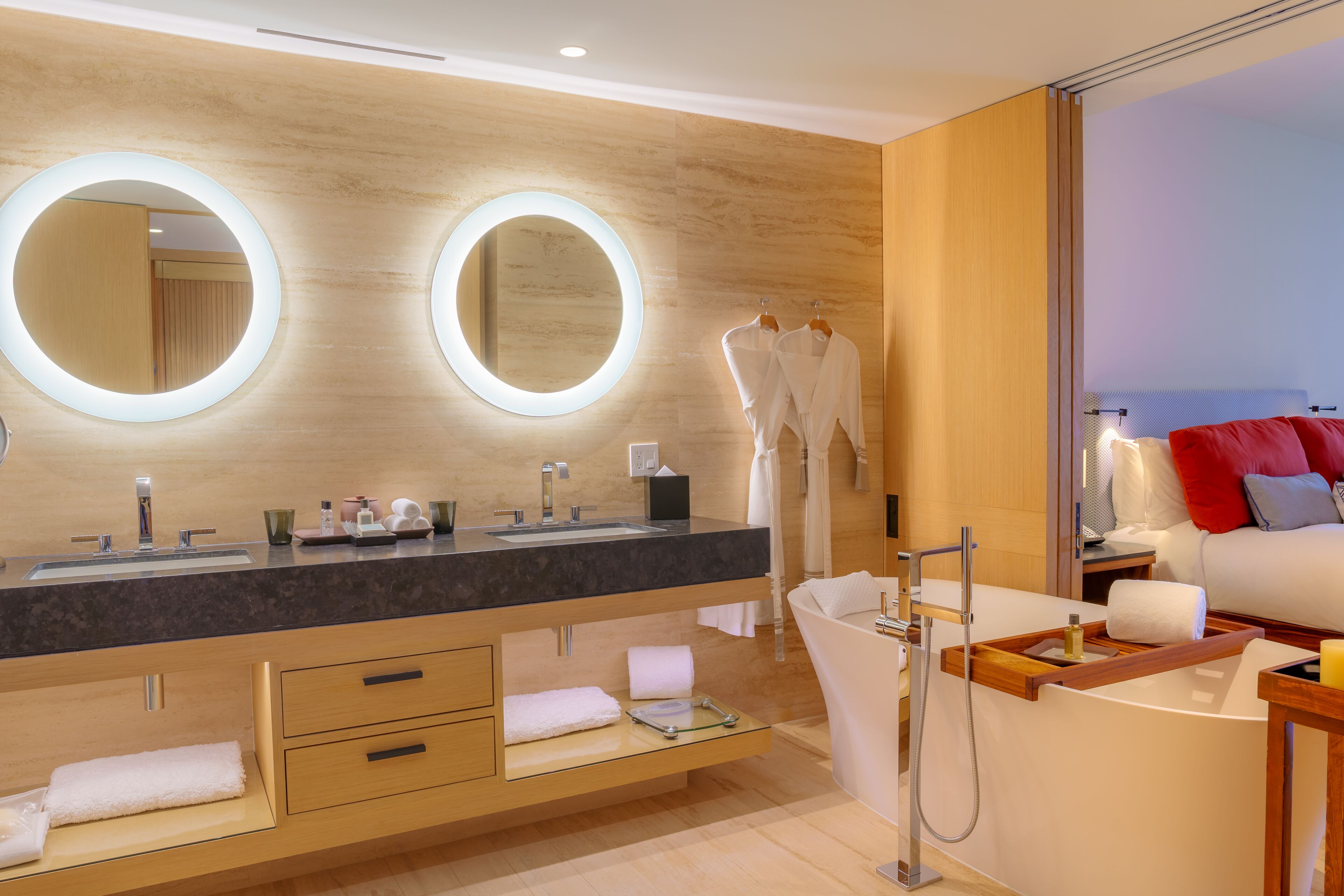 A modern bathroom with a large mirror, dual sinks, and a bathtub.