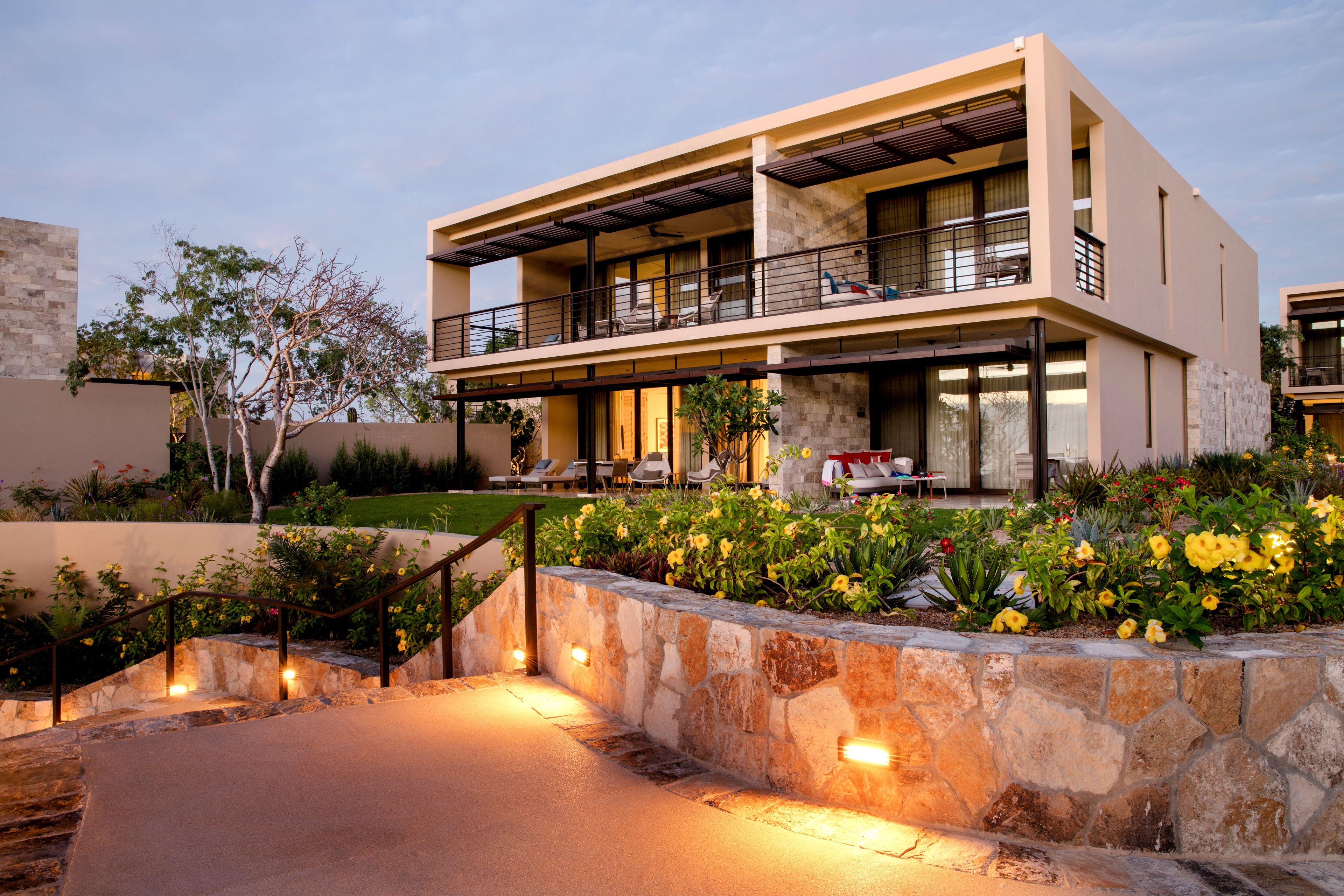 A modern two-story house with a stone retaining wall, a balcony, and a well-lit entrance.