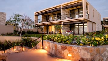 A modern two-story house with a stone retaining wall, a balcony, and a well-lit entrance.