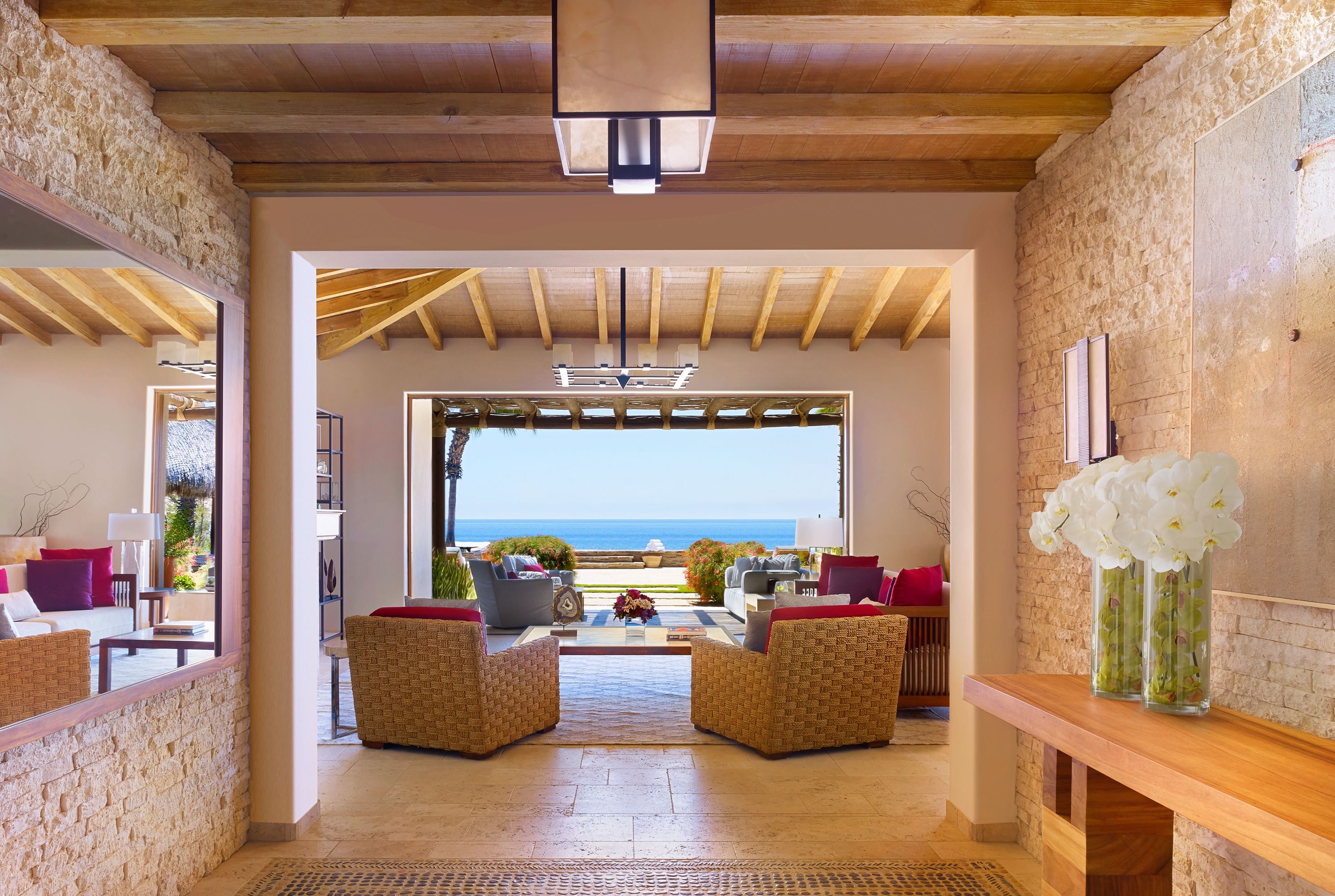 A spacious lobby with wicker furniture, a wooden ceiling, and a view of the sea.