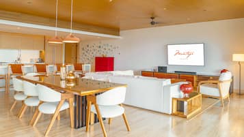 A modern living room with a wooden dining table, white chairs, a red accent wall, and a flat-screen TV.