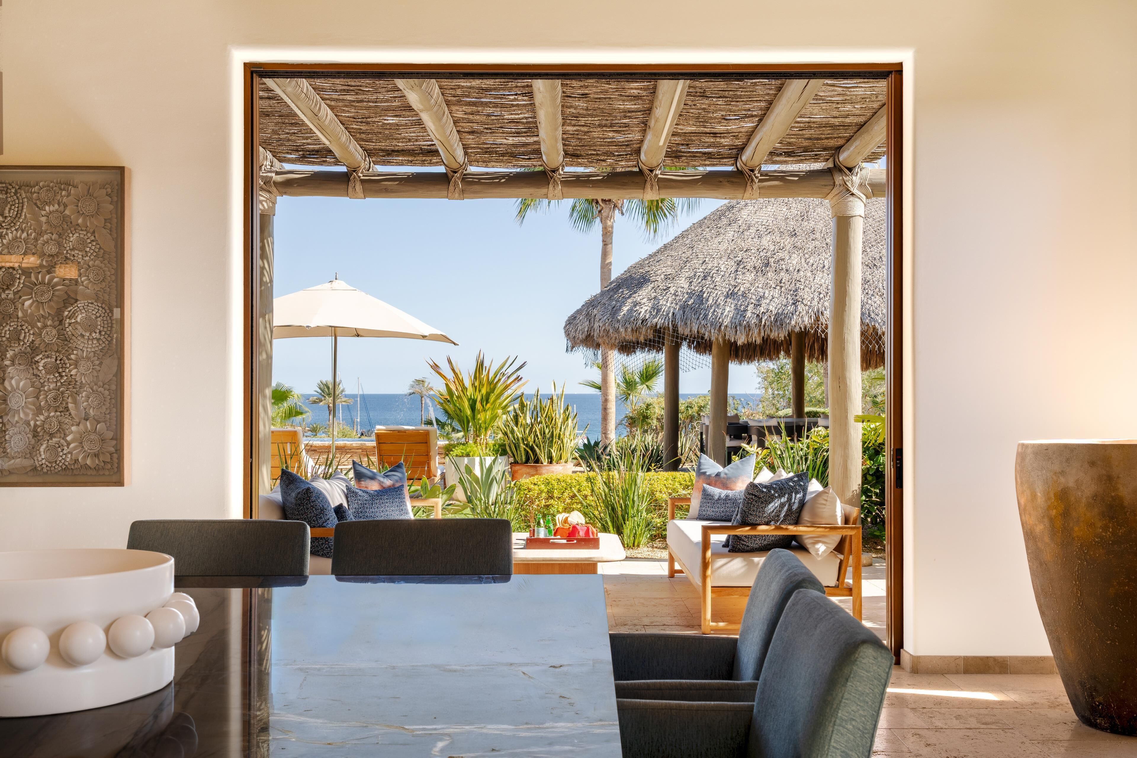 Un espacio moderno con asientos al aire libre y vistas al océano, una estructura con techo de paja y una gran maceta decorativa.