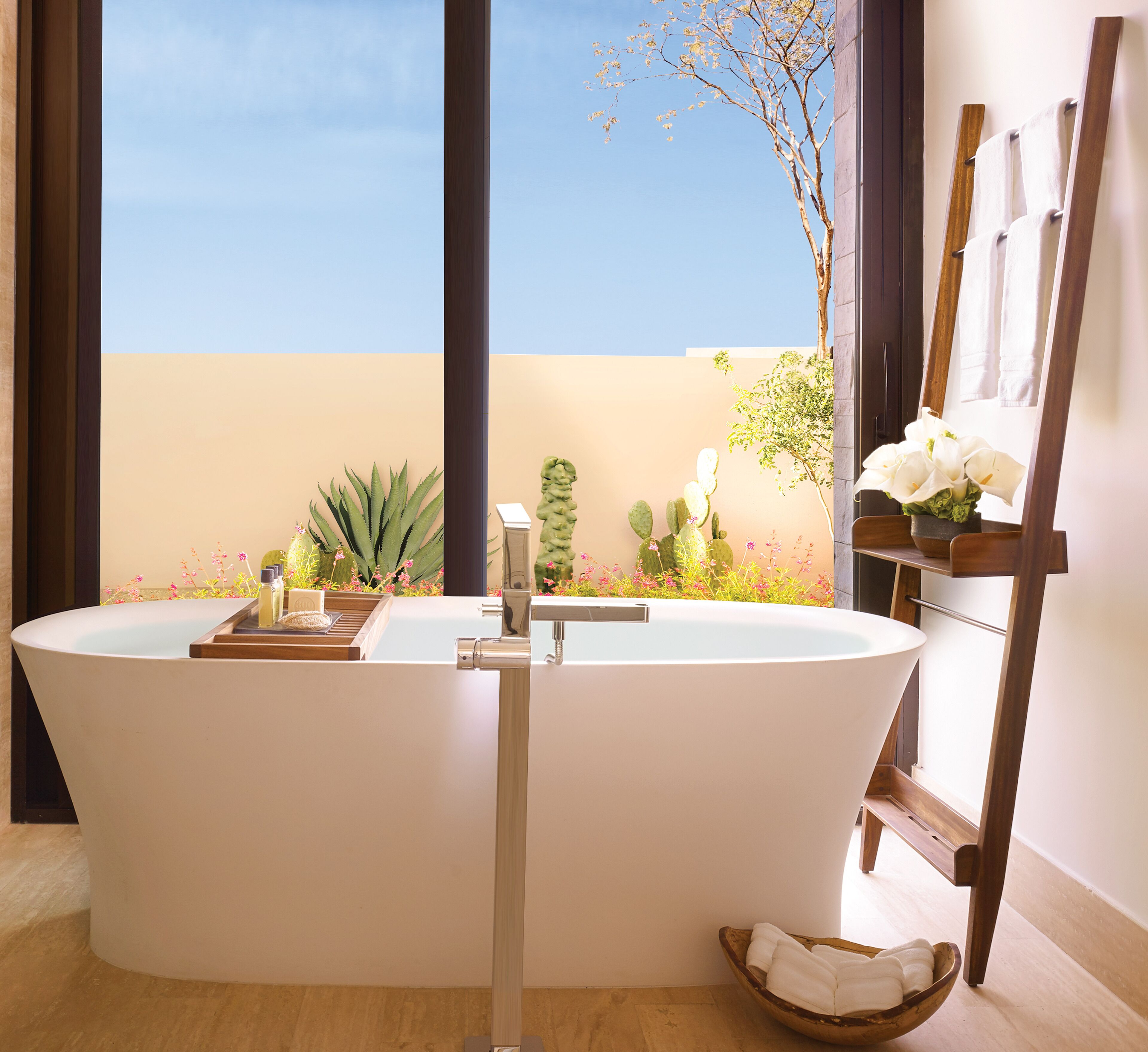 A modern bathroom with a freestanding bathtub, a wooden side table, and a small plant.