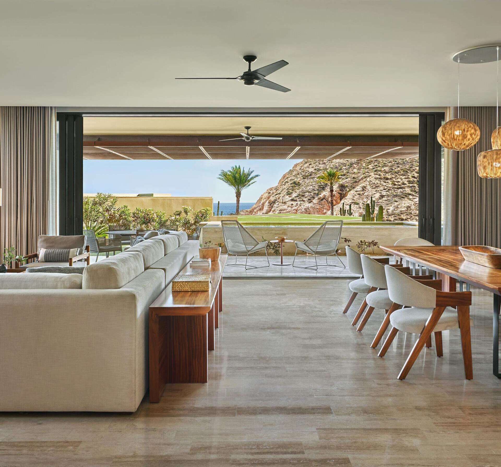 A spacious living area with a large sofa set, a dining table with chairs, and a view of a rocky landscape and ocean.