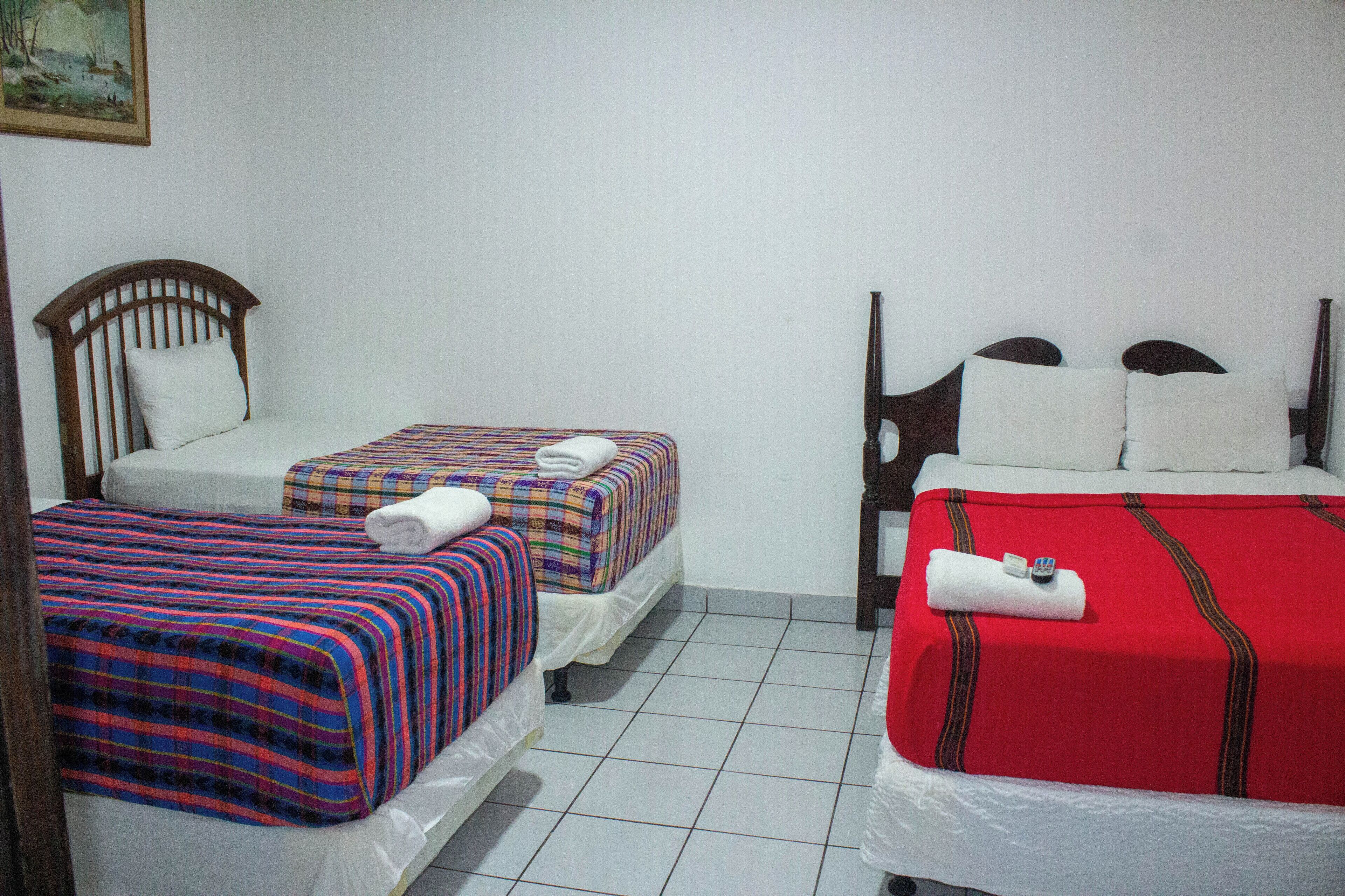 A hotel room with two beds, each with a different patterned bedspread, and a red bedspread on the right.