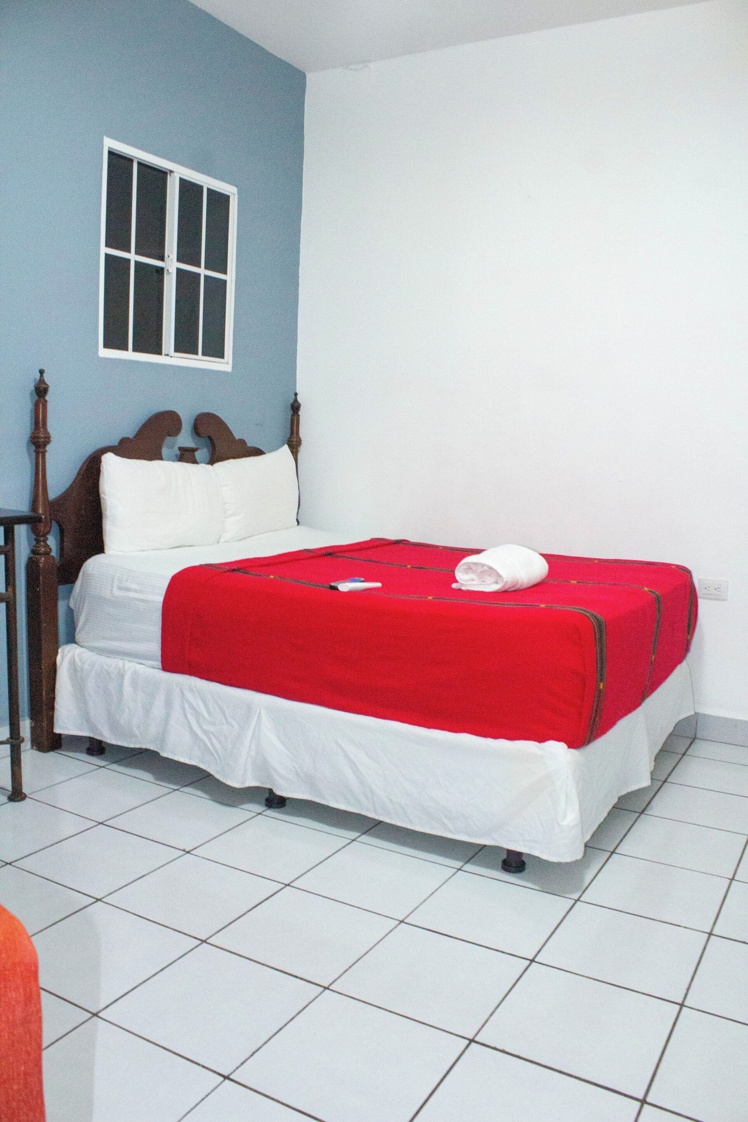Uma cama de solteiro com manta vermelha, roupa de cama branca e cabeceira de madeira.