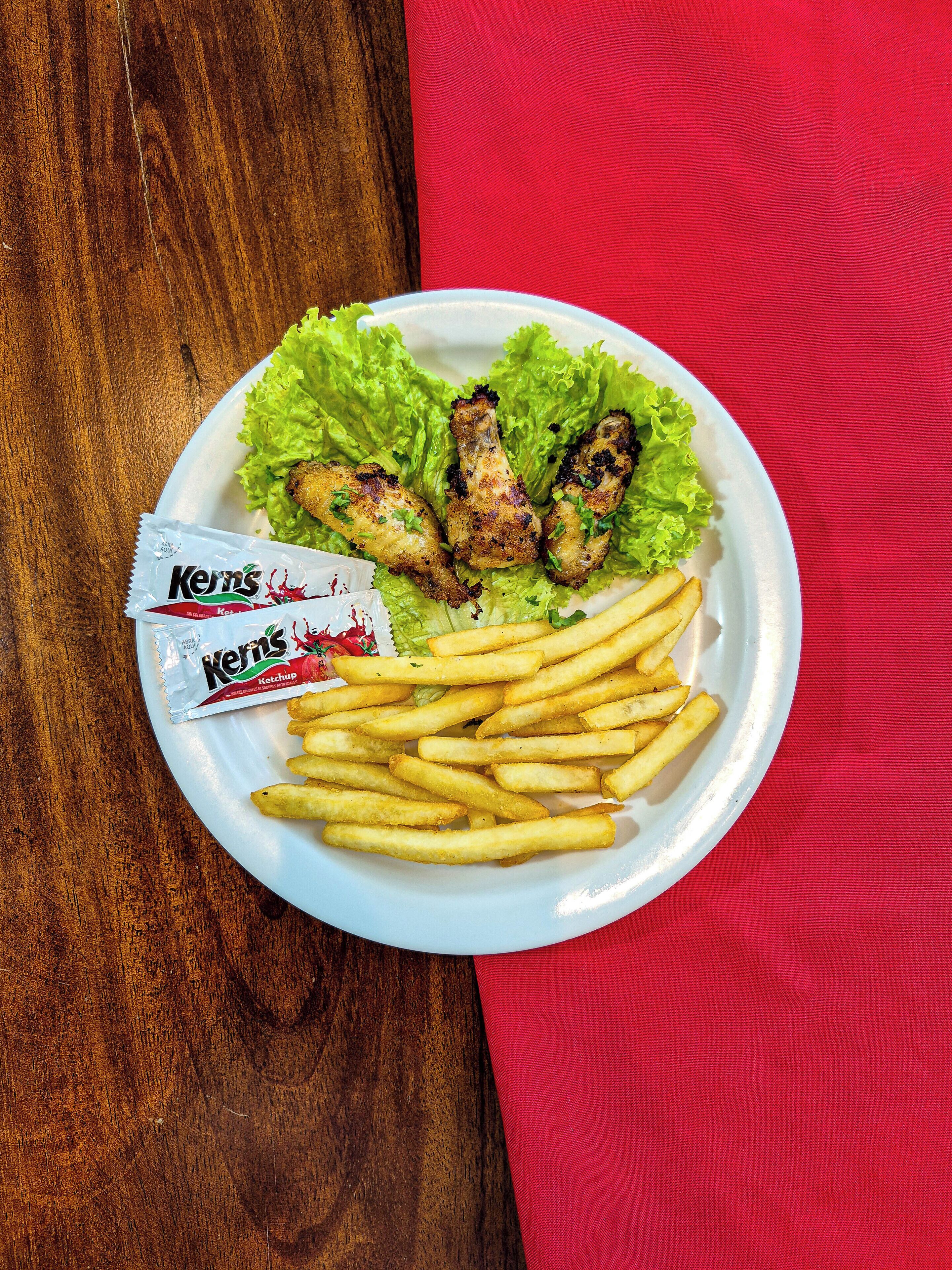 Un plato con alitas de pollo, papas fritas y lechuga sobre una mesa de madera con un mantel rojo.