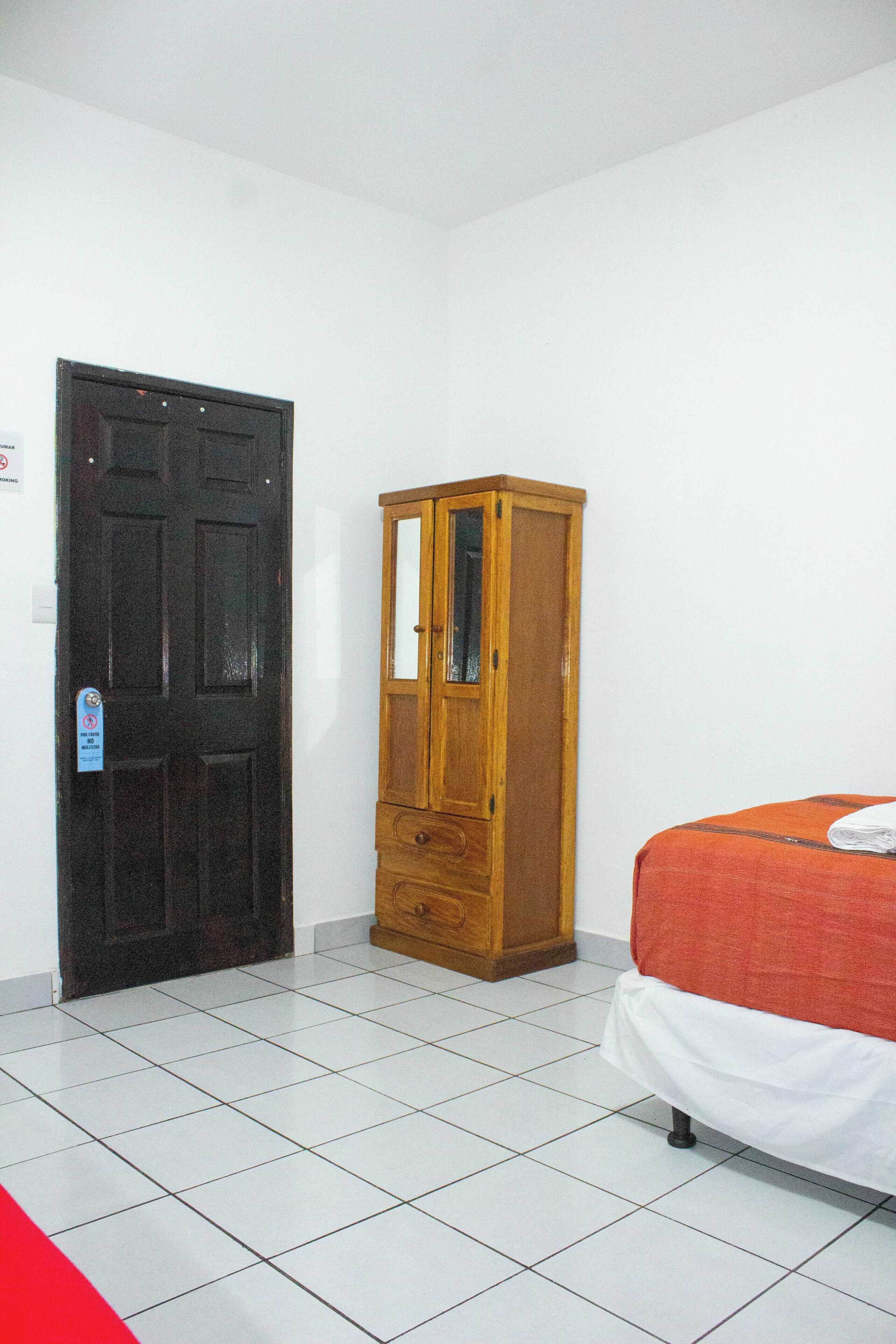 Una habitación con una puerta cerrada, un armario de madera y una cama con una colcha roja.