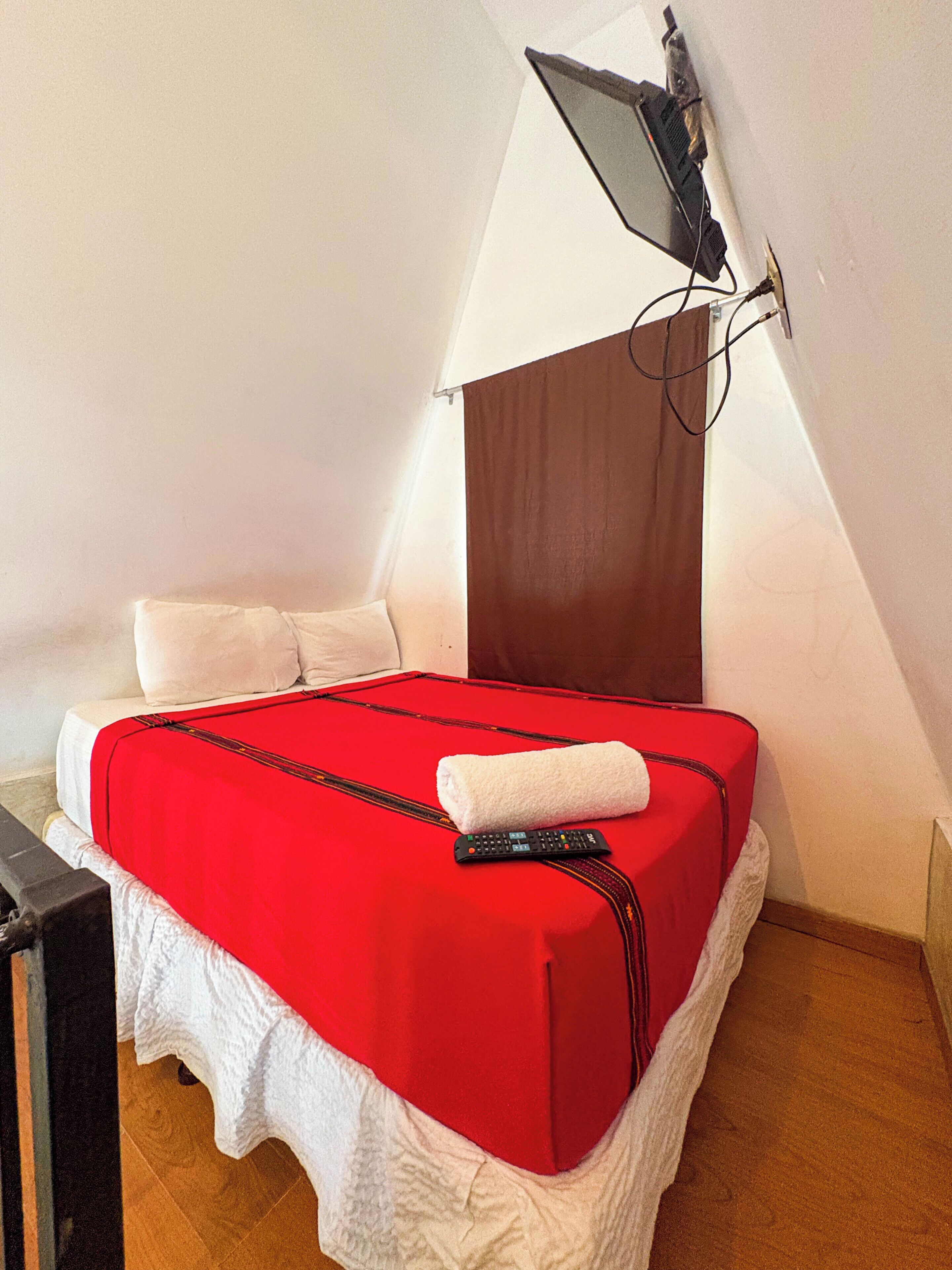 Un lit avec une couverture rouge, une télécommande et une serviette blanche.