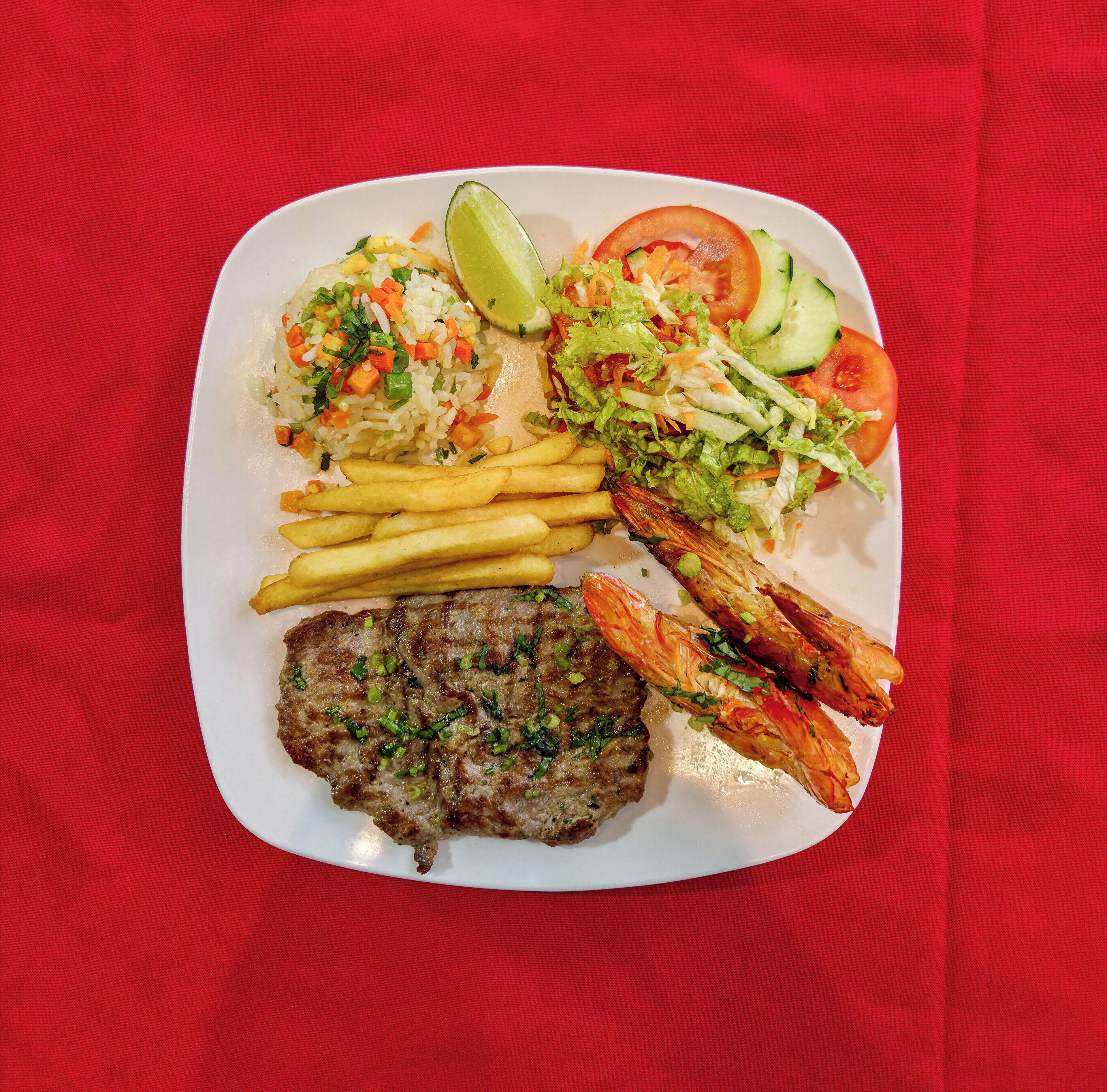Un plato con arroz, papas fritas, camarones, un bistec y una ensalada.