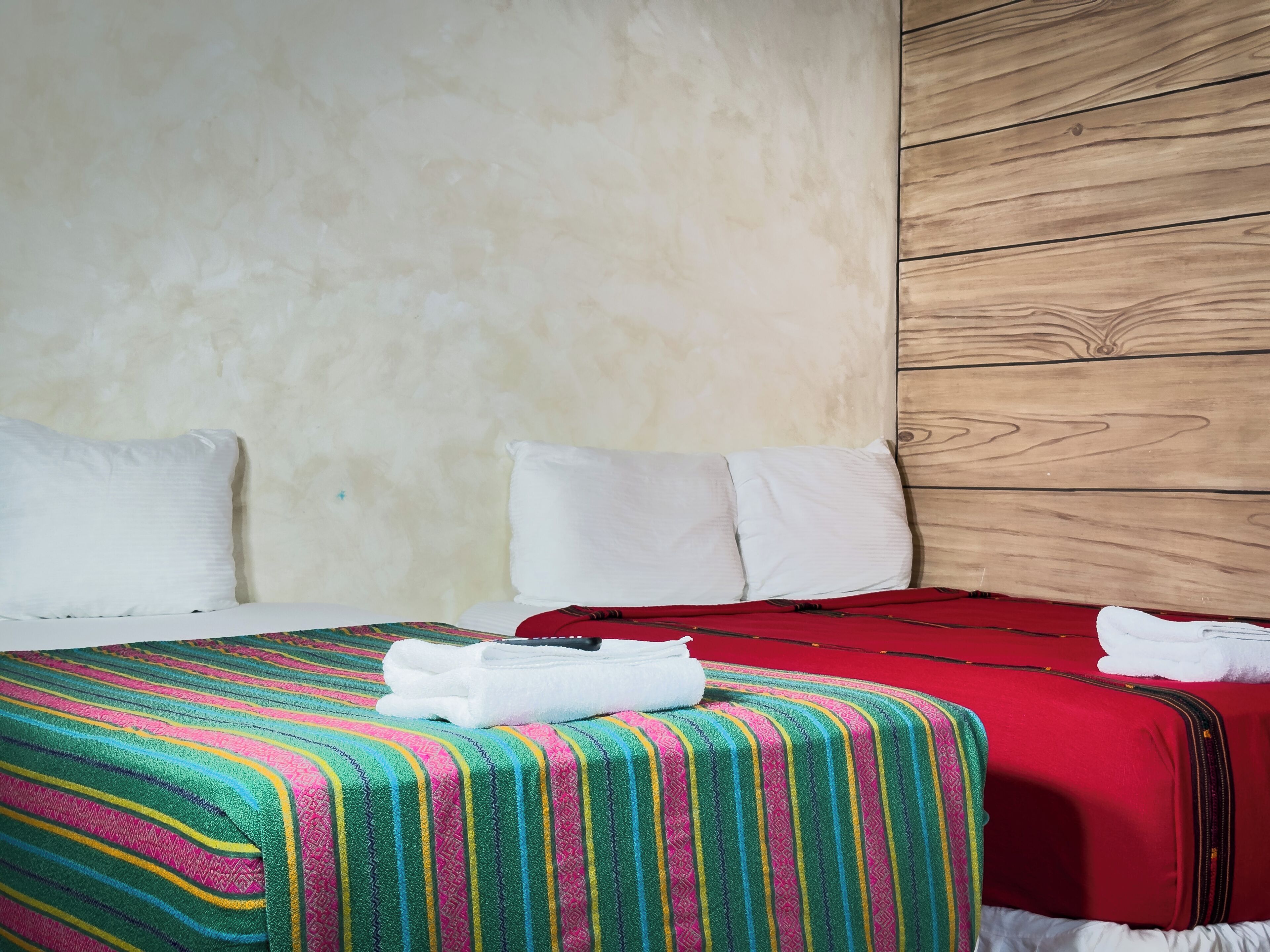 A hotel room with a bed, two pillows, a colorful striped blanket, and a red suitcase.
