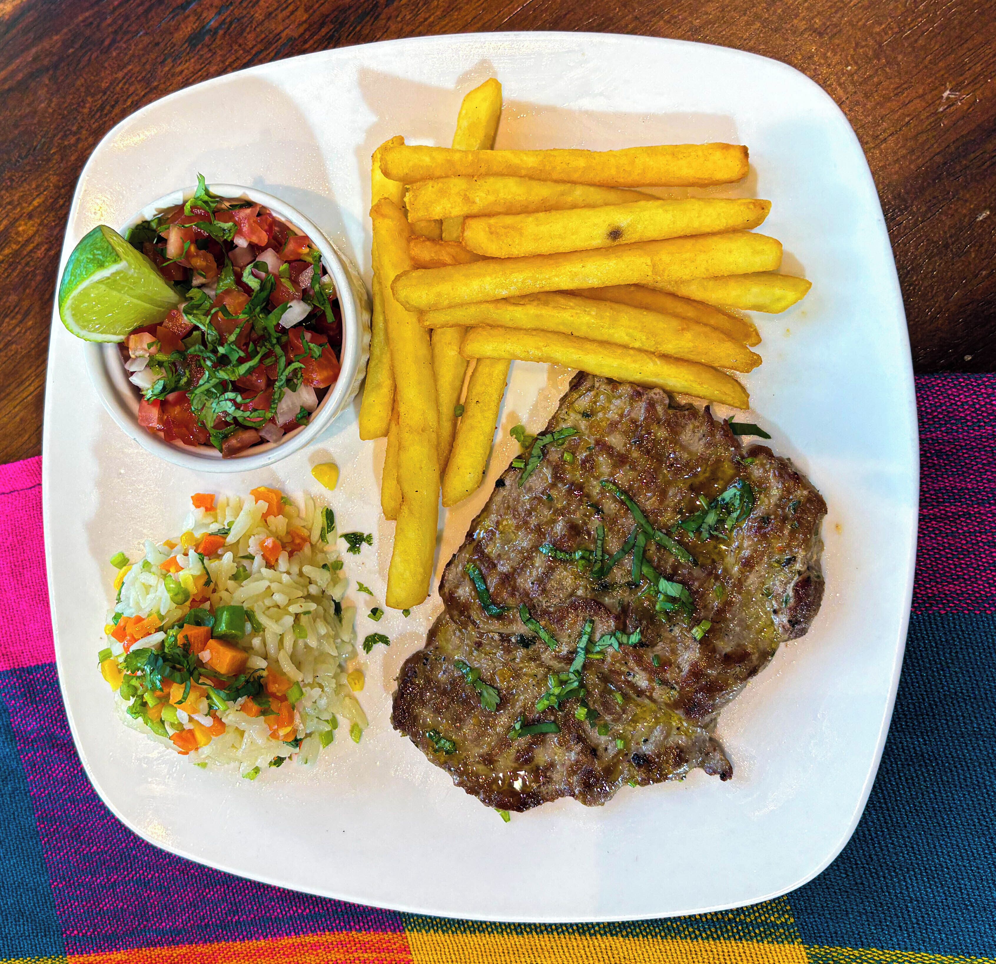 A plate with a steak, fries, and a side of rice and salsa.