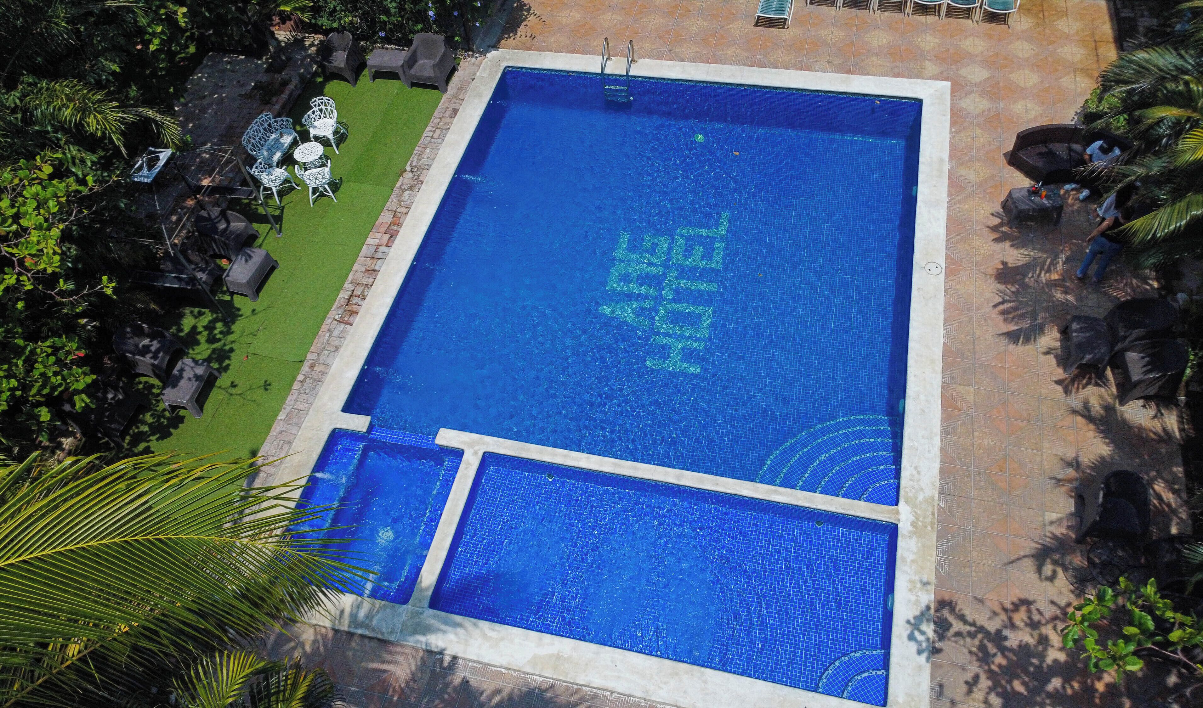 A rectangular swimming pool with a tiled edge, surrounded by a patio area with chairs and tables.