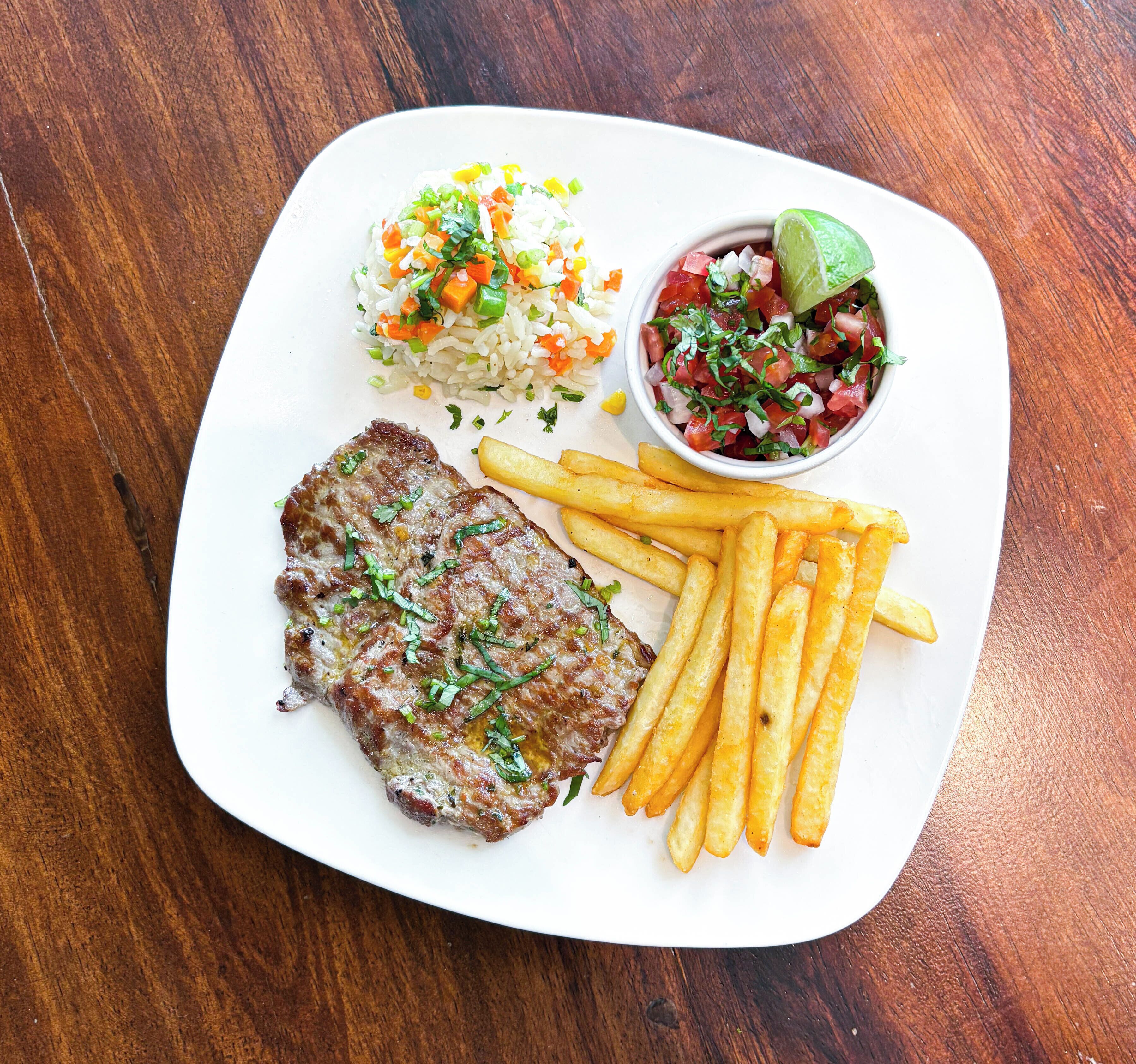 Une assiette avec un steak, des frites, du riz et un bol de salsa.