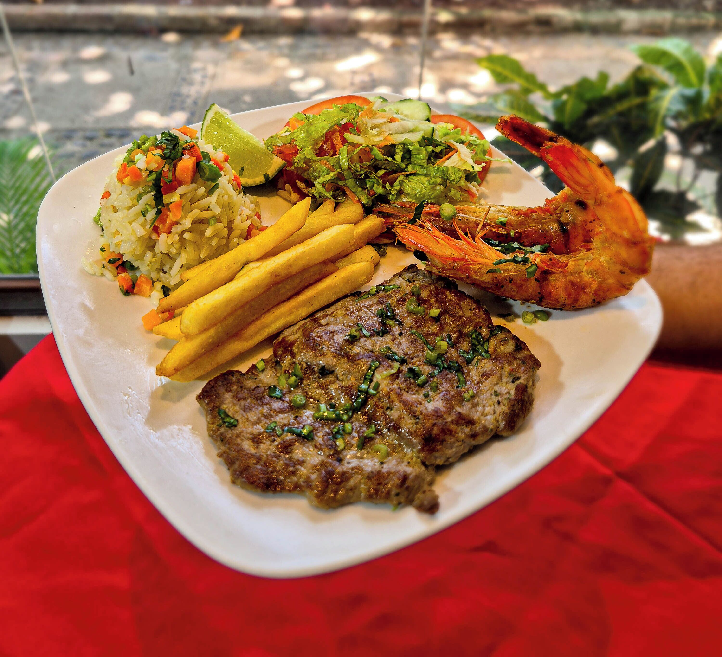 A plate with a steak, shrimp, fries, and a salad.