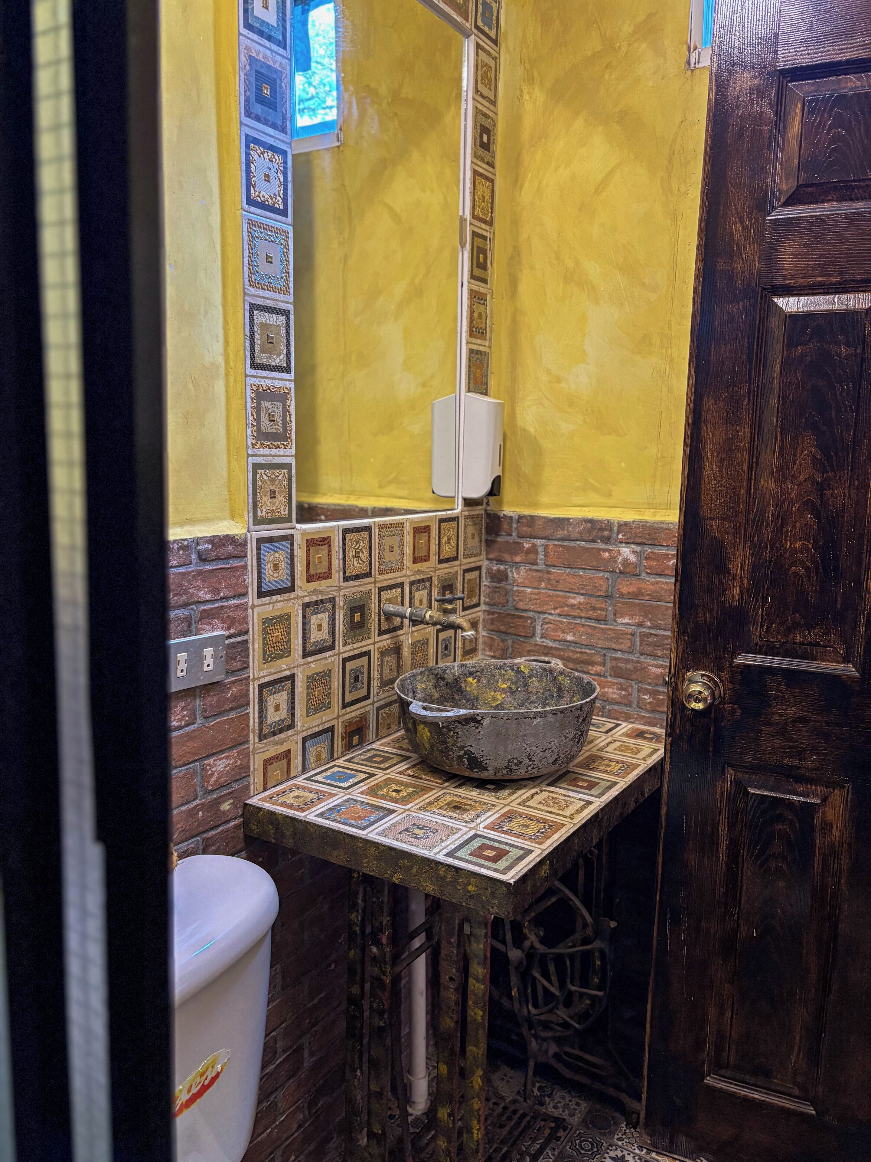 Ein Badezimmer mit einem gefliesten Waschbecken, einer Toilette und einer Holztür.